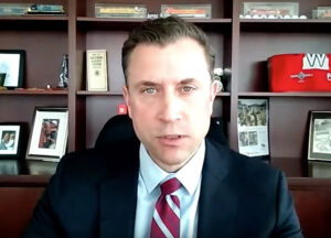 Man with dark suit and tie with bookshelves in background