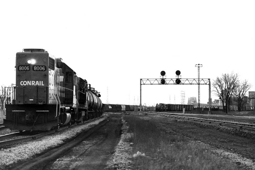 Conrail freight train at left while second train approaches in distance under signal bridge