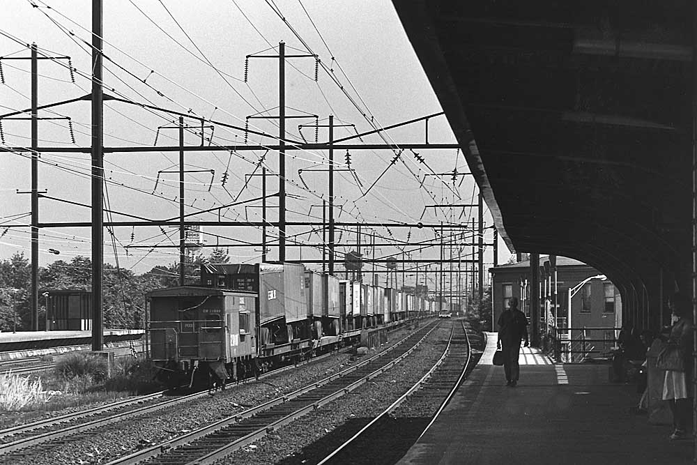 Rear of Conrail freight train with trailers on flatcars passing station on electrified trackage