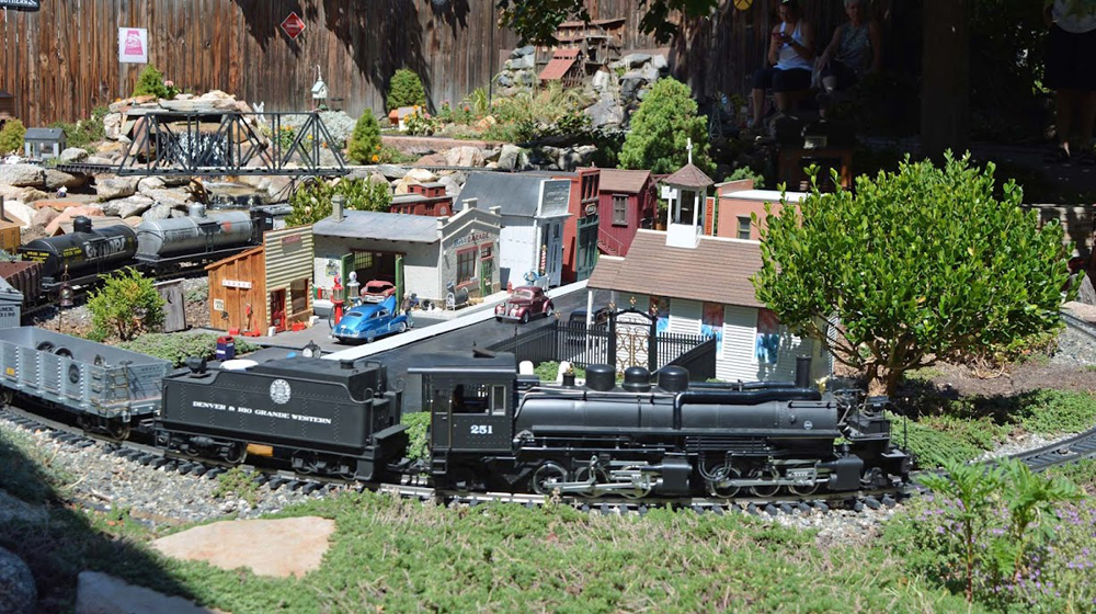 Model steam locomotive passes by a town