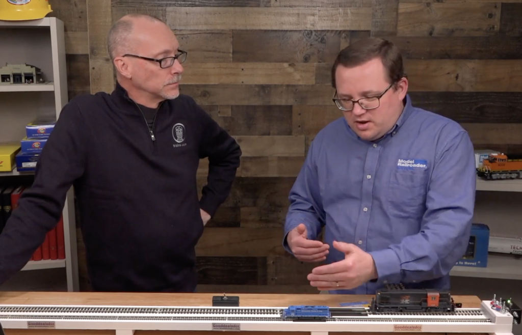 Two men talking at a table over a model train.