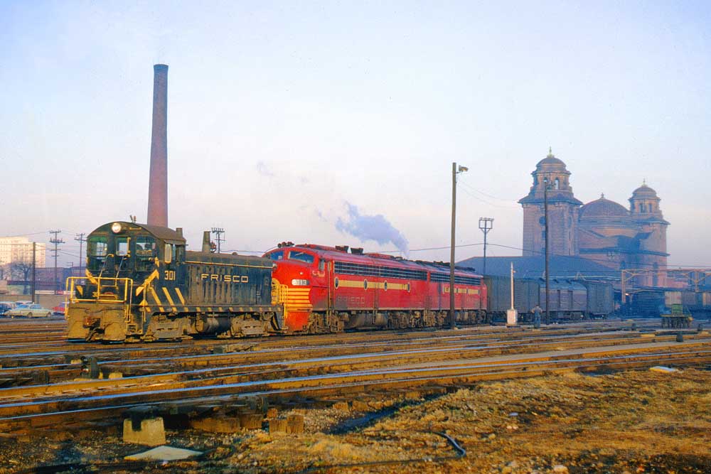 Black and yellow diesel locomotive pulls two red and yellow diesel locomotives and passenger cars