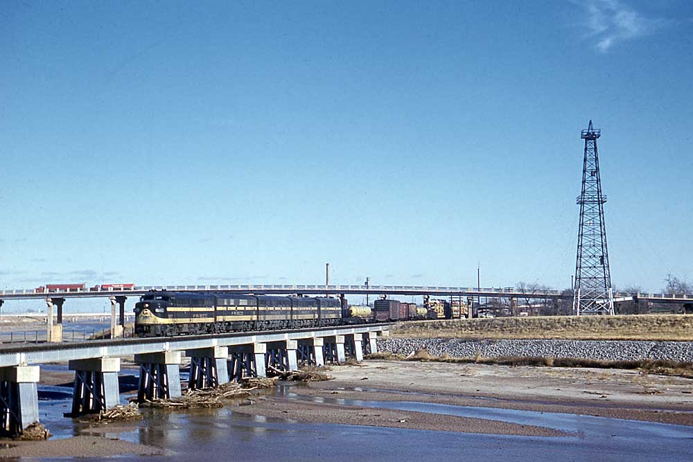 Black and gold diesel locomotives with Frisco freight train on low bridge