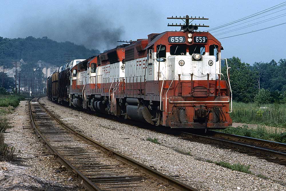 Three red and white diesel locomotives on a Frisco freight train with automobile loads