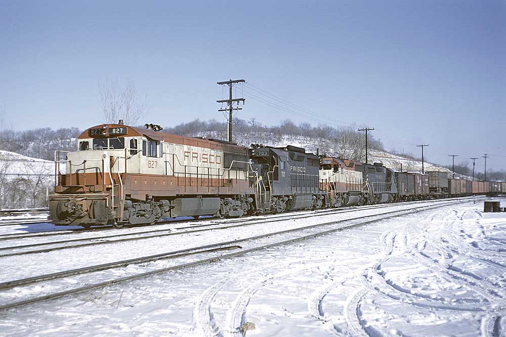 Two red and white and two black and yellow diesel locomotives on a freight train in snow