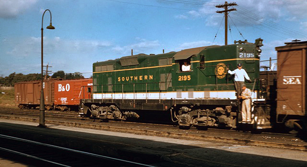 Green and white locomotive with railroad workers on the front.