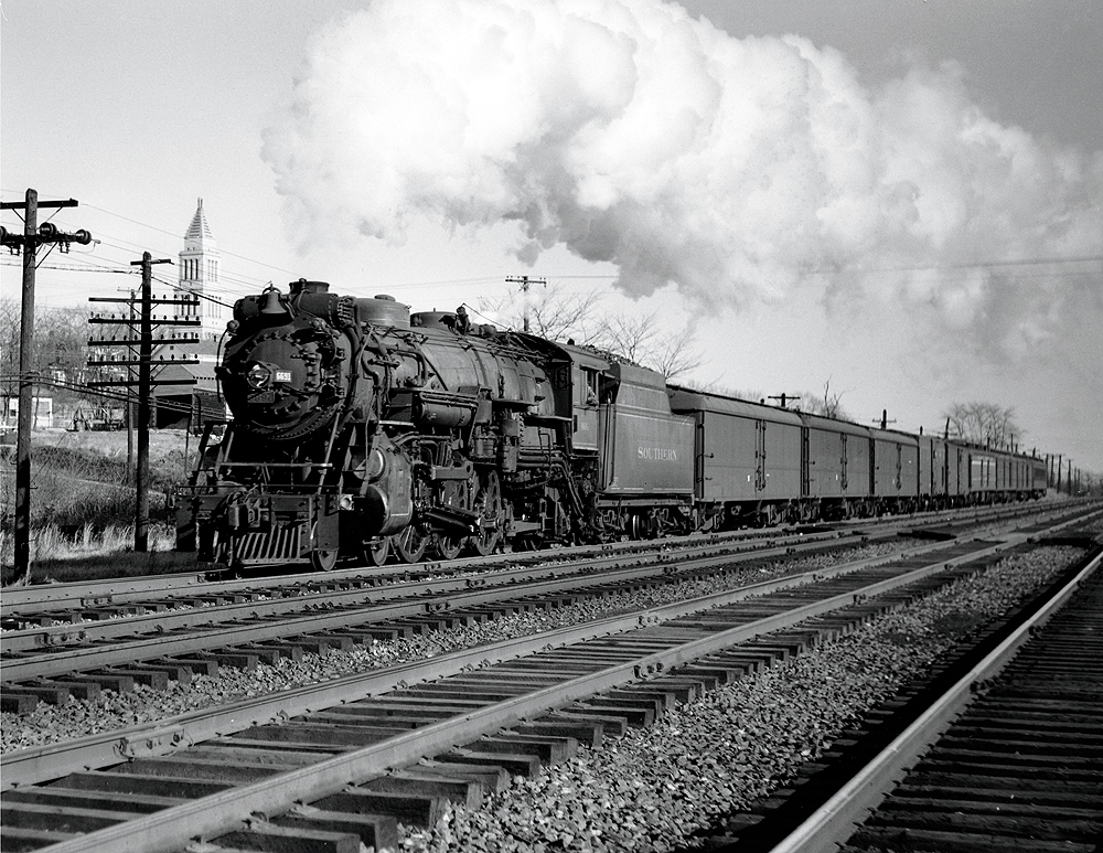 Steam locomotive with white plume hauling a long passenger train