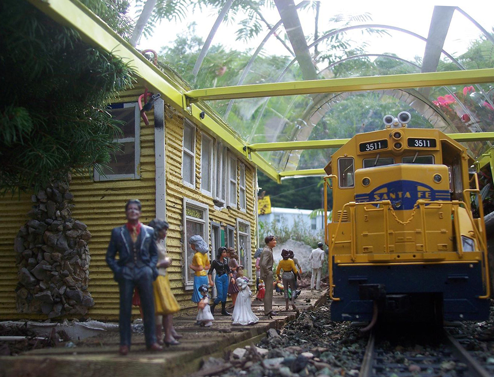 Model diesel locomotive pulls up to a model station with figures