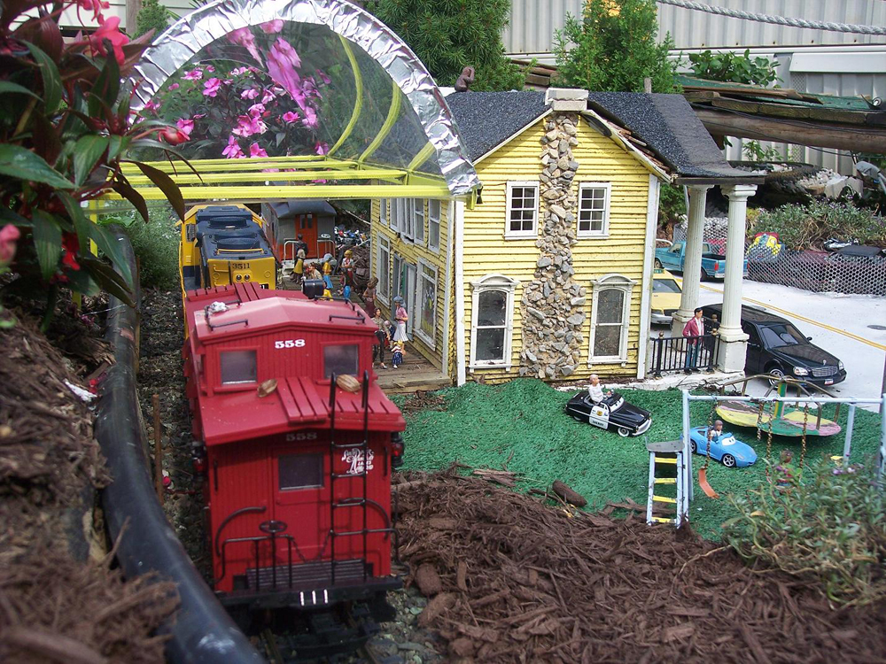 Model train caboose with yellow structure on a garden railway