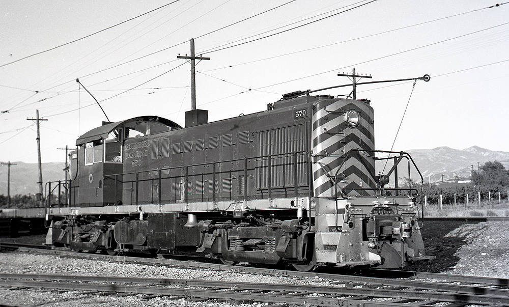 Black and white switcher locomotive with trolley pole.