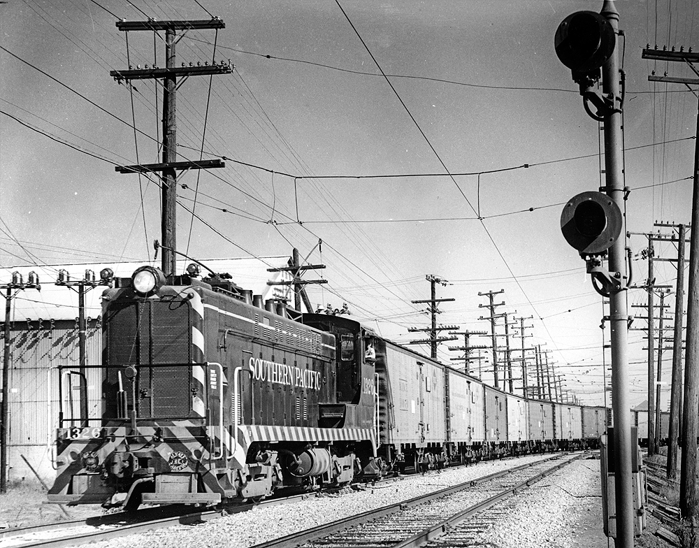 Baldwin locomotive with trolley pole extended pulling refrigerated boxcars.