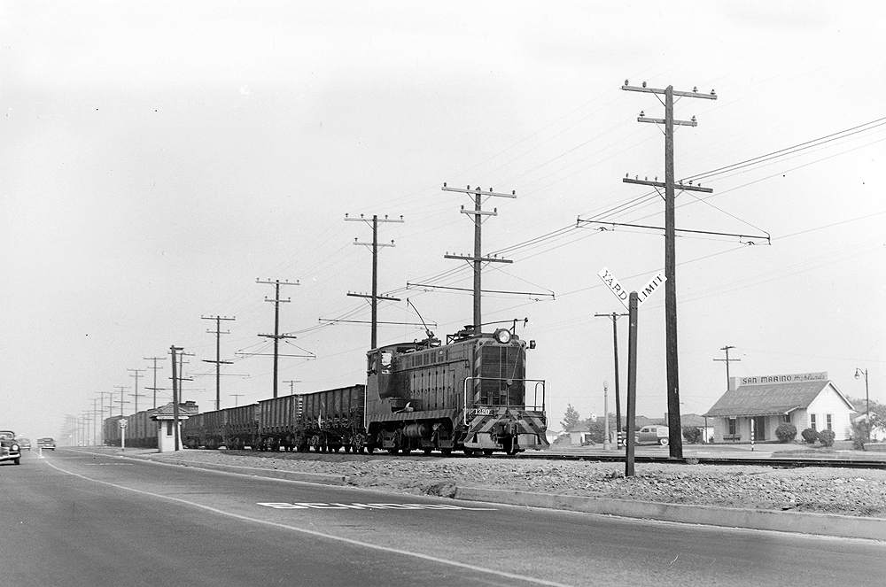 Baldwin locomotive with trolley pole extended pulling freight train.