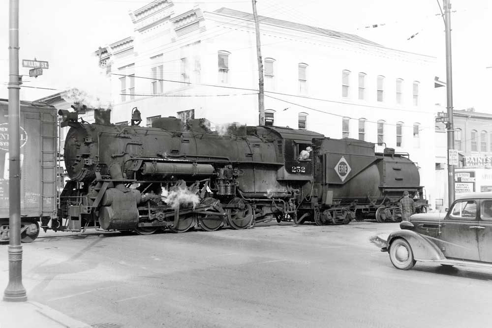Steam locomotive in profile in street crossing
