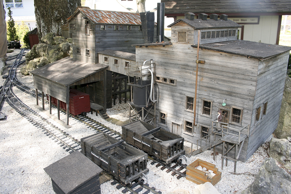 Coal and lumber garden railroad: Model coal cars next to a power station on a garden railway