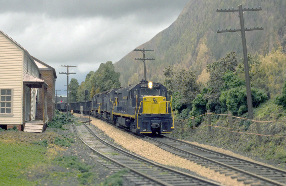 A blue C&O diesel with a yellow nose leads an ore train through an Appalachian landscape
