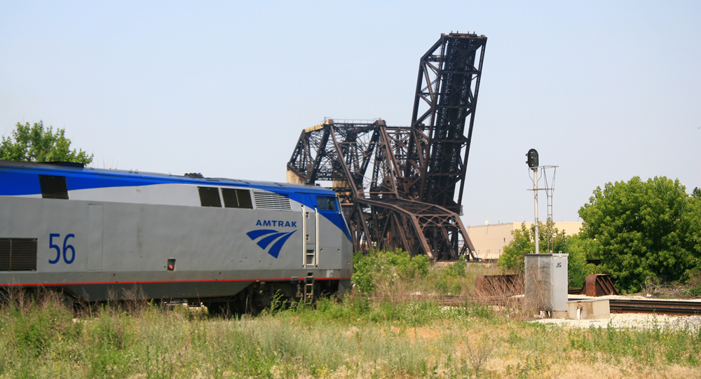 Locomotive approaches signal with raised bridge in background