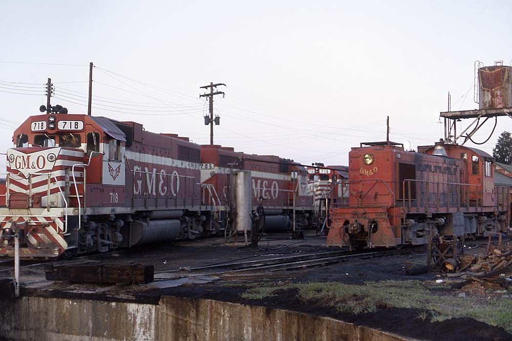 Red and white diesel locomotives next to all-red diesel locomotive beside turntable pit