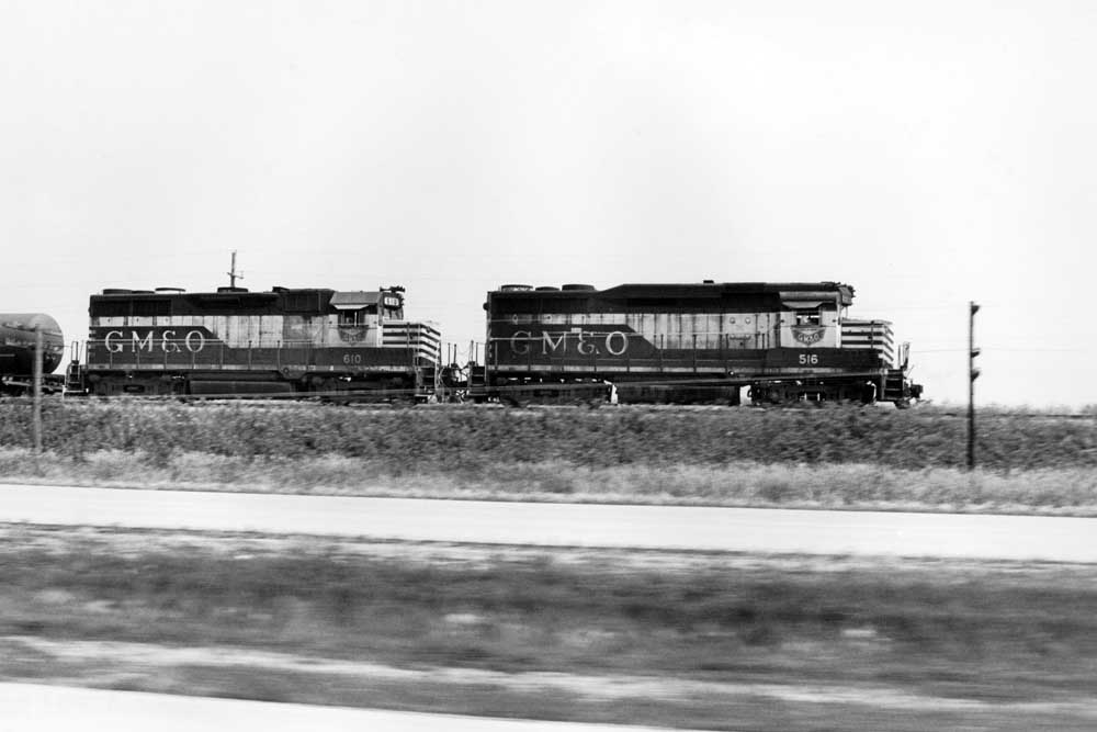 Black and white diesel locomotives race traffic along a highway