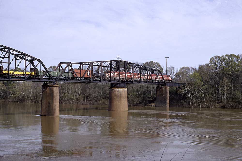 Red and white diesel locomotives with freight train on truss bridge over river