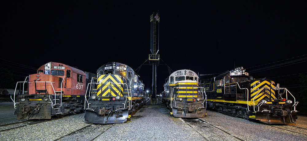 Four locomotives lined up side-by-side in a nighttime photo event.