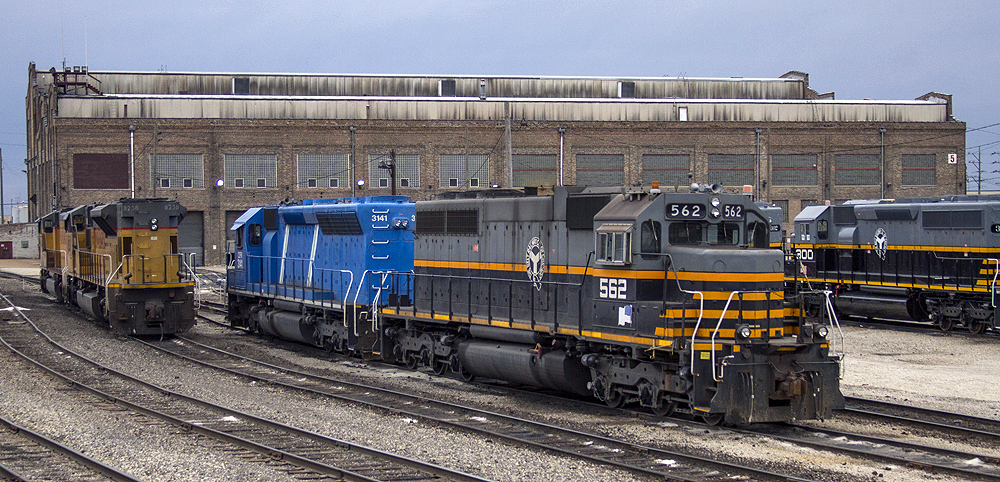 Yellow, blue, and gray-and-black diesel locomotives in a rail yard.