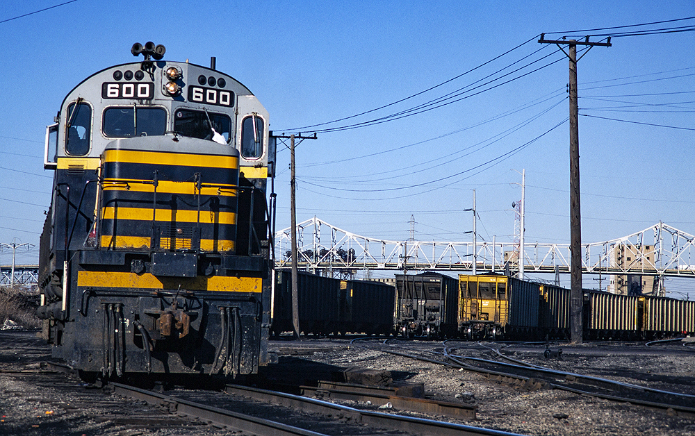 Close nose-on image of a black, yellow, and gray diesel locomotive in a rail yard.