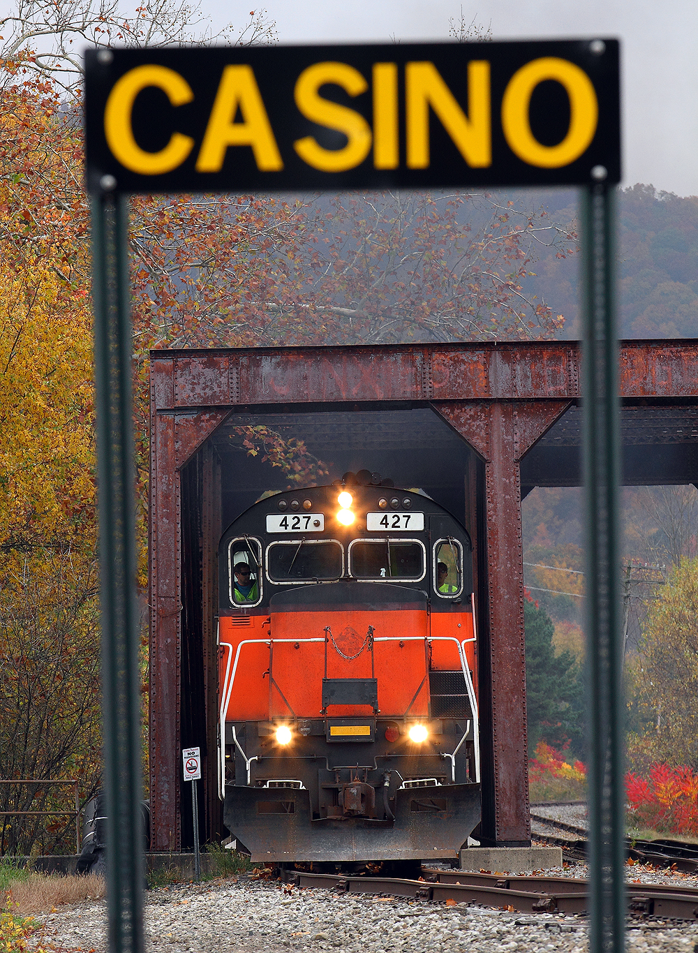 Red-and-black locomotive pictured through a near foreground sign post.