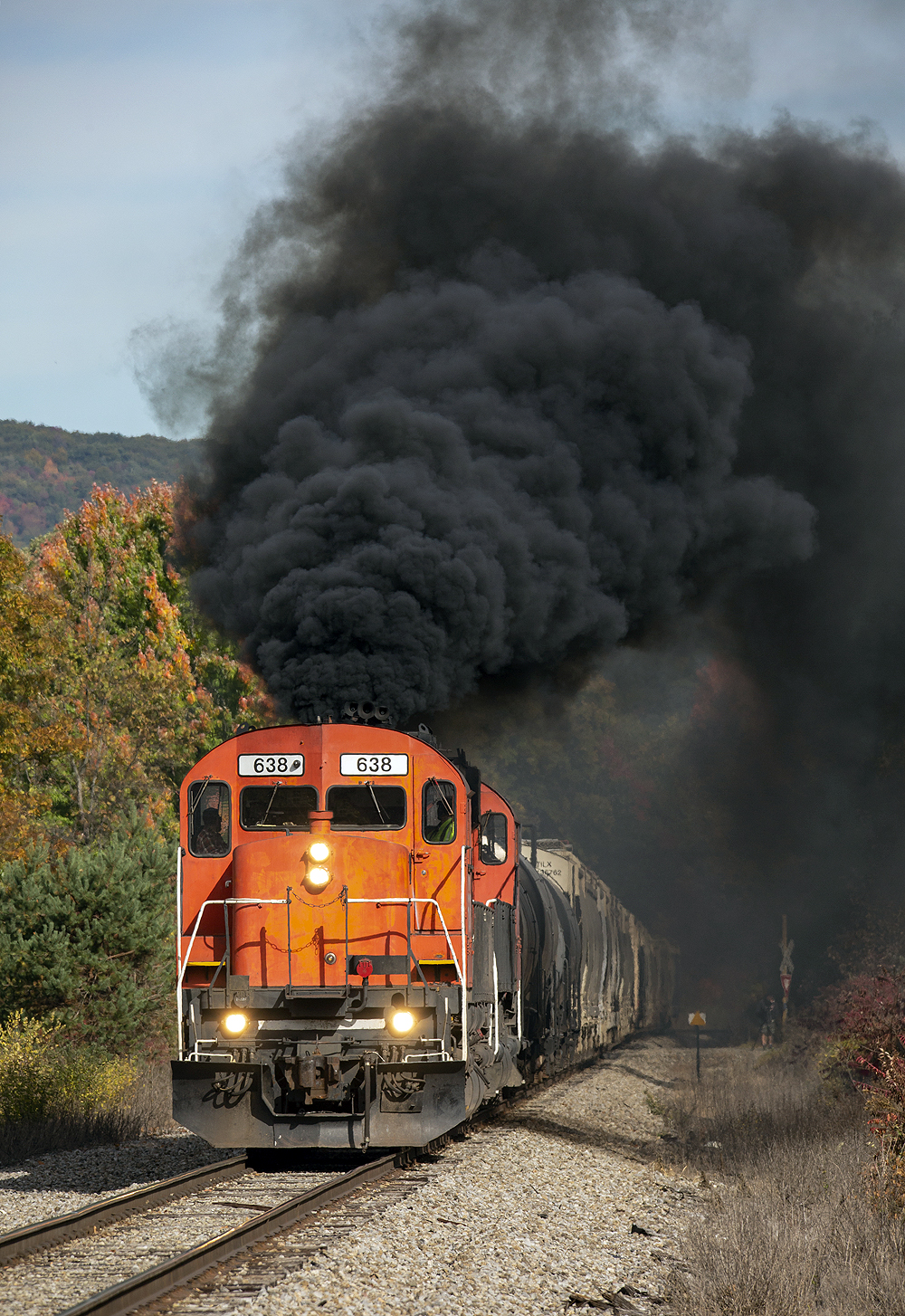 A red locomotive belches black smoke into a colorful autumnal scene.