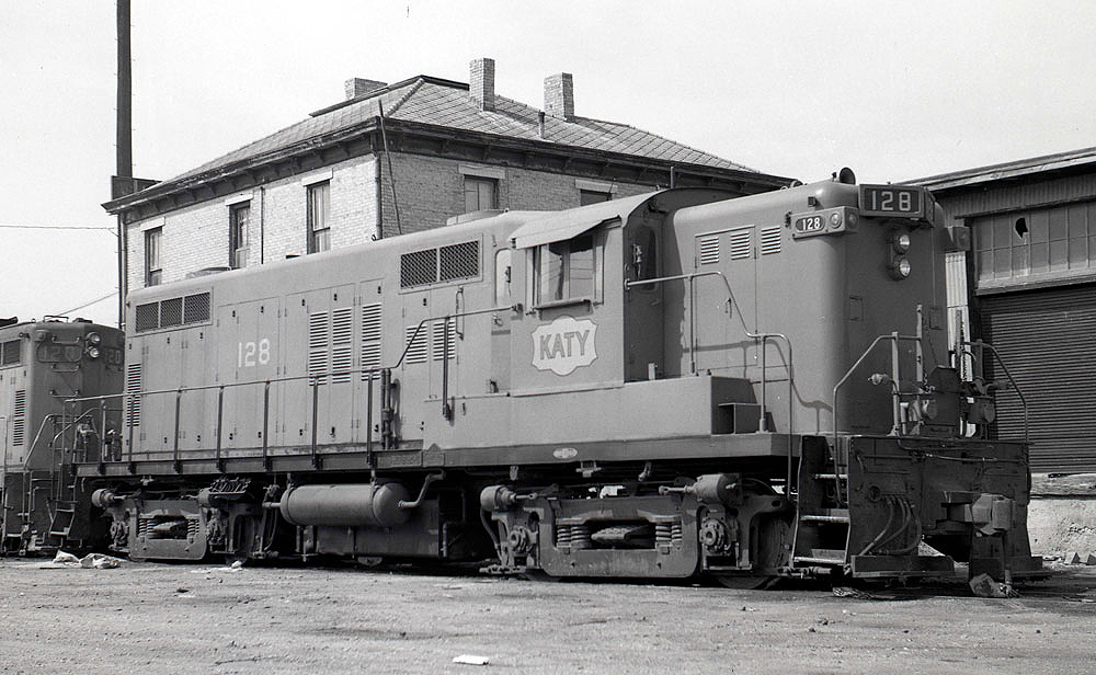 Black and white image of a locomotive near a building.