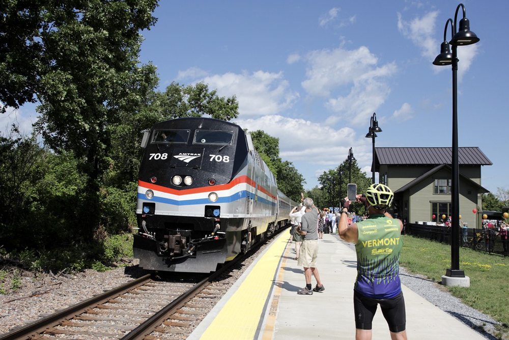 Passenger train arrives at station arrives with crowd on platform.