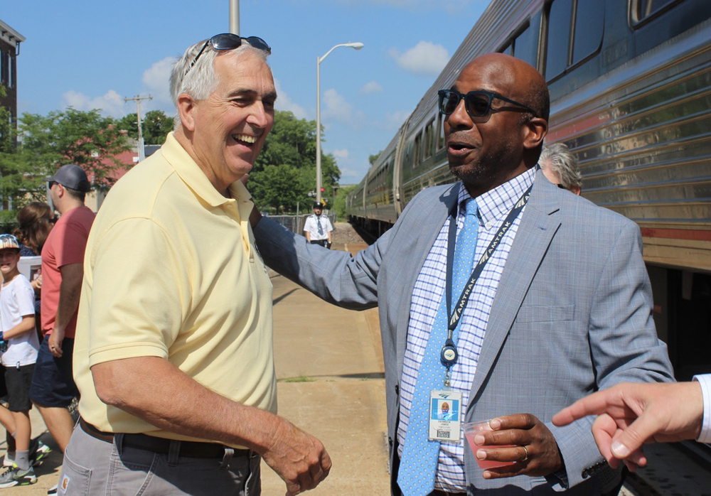 Smiling man in yellow shirt talking with smiling man in gray suit