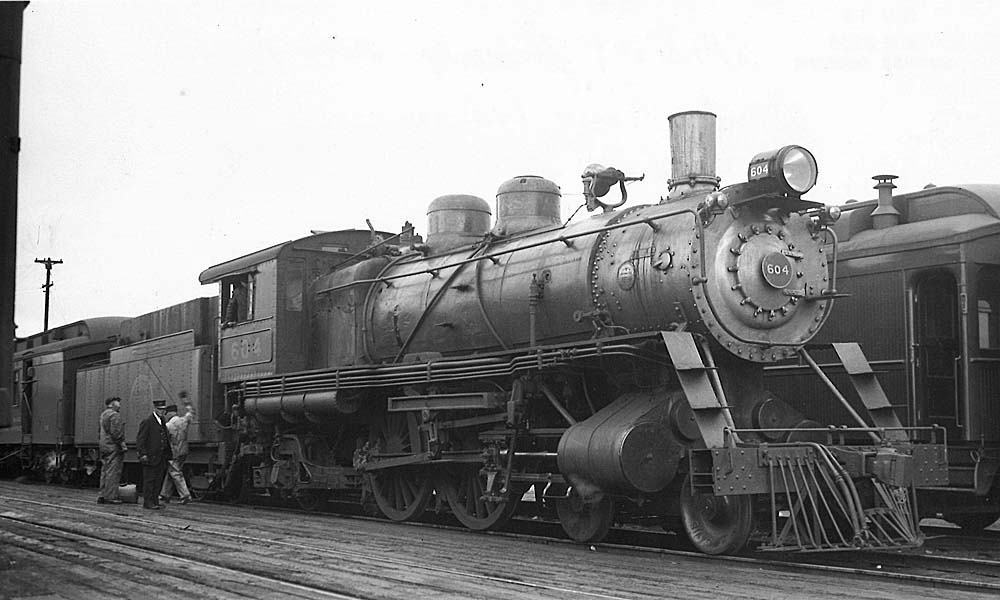 Men standing by steam locomotive tender on passenger train
