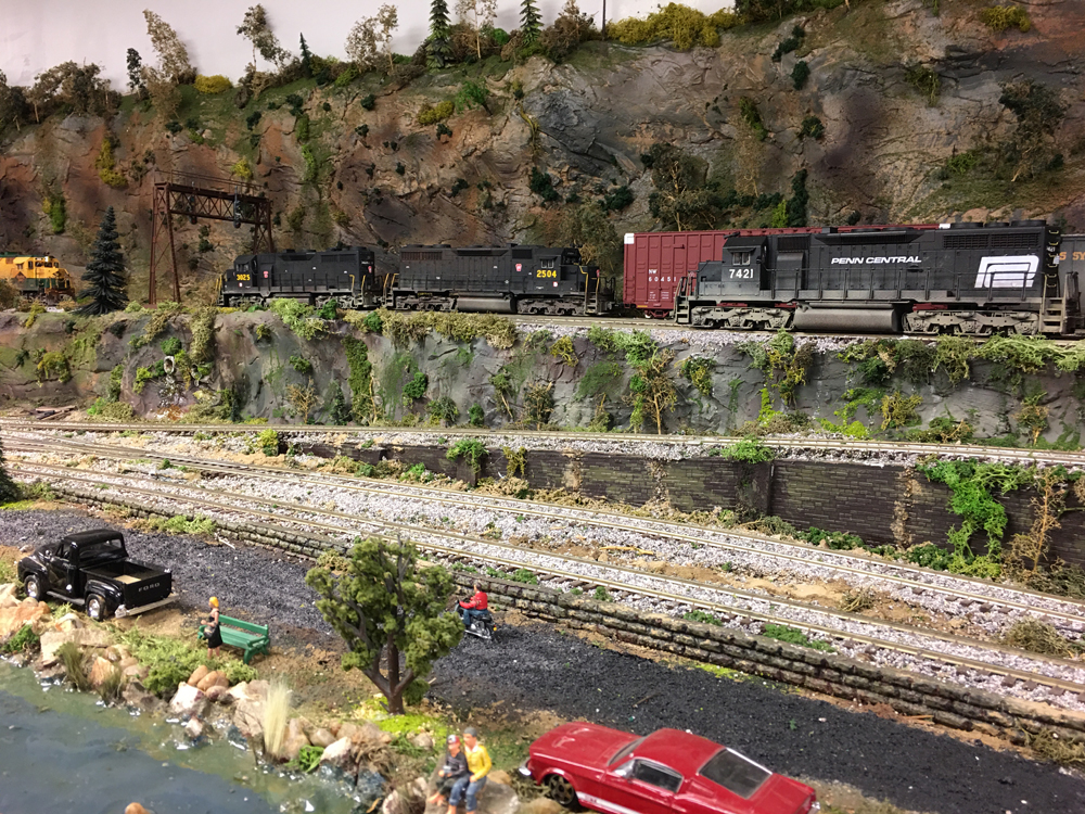 People fish in a pond while on the other side of a rail yard diesels wait for another train to pass