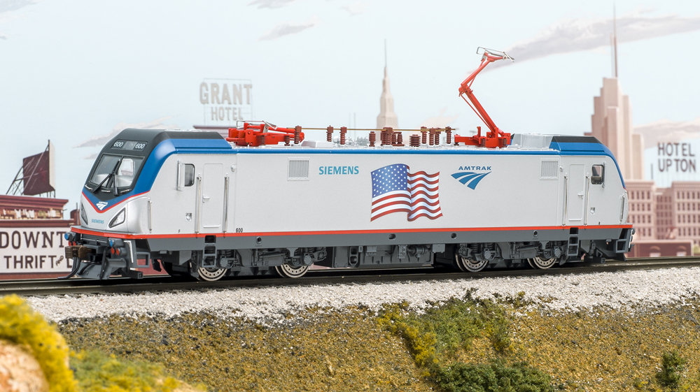 Photo of HO scale electric locomotive on scenicked base with cityscape background