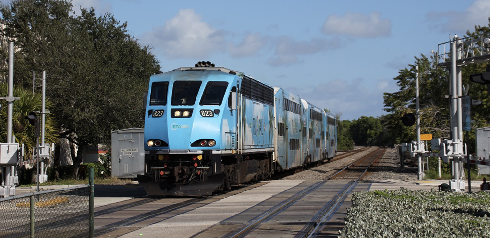 Light blue locomotie with bilevel commuter cars crossing street