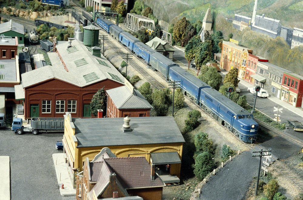 A passenger train passes through a town and industries on an HO scale model railroad