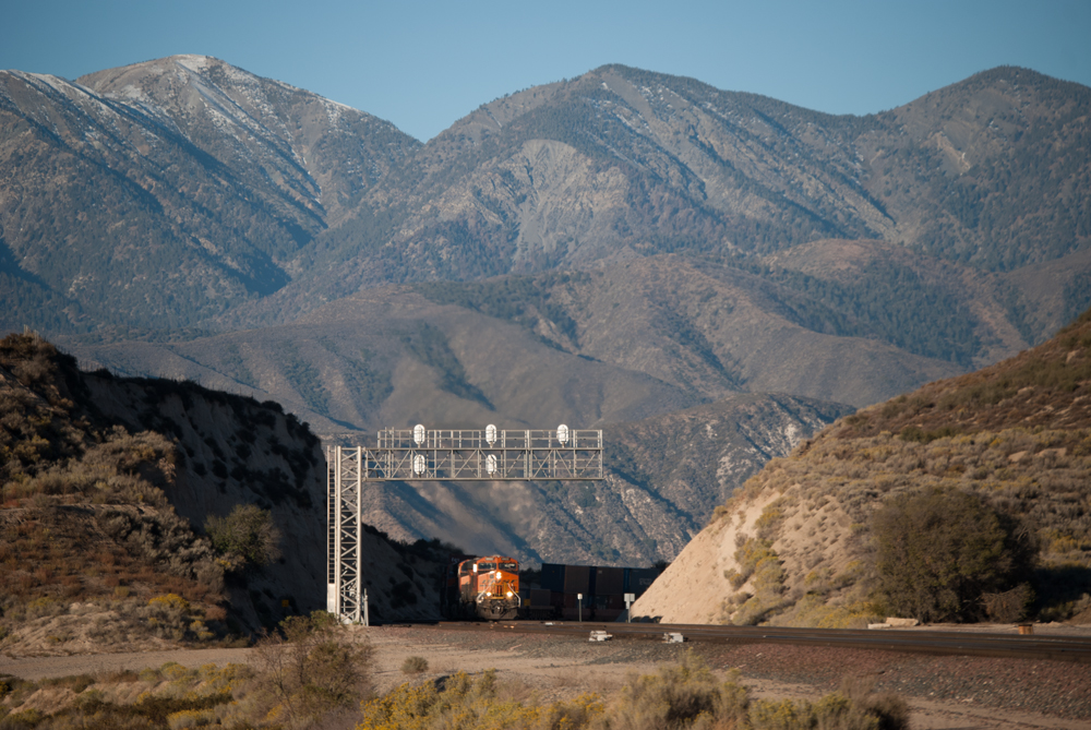 Wide-field image of an orange locomotive in a barren mountain scene.