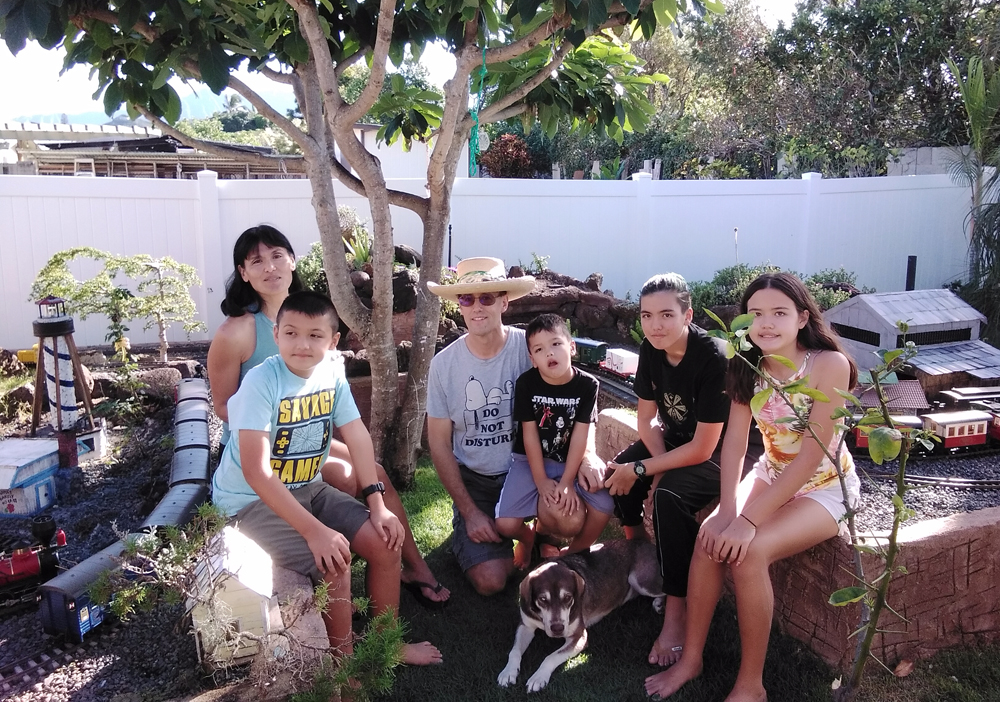 Two adults and four children pose near a garden railway