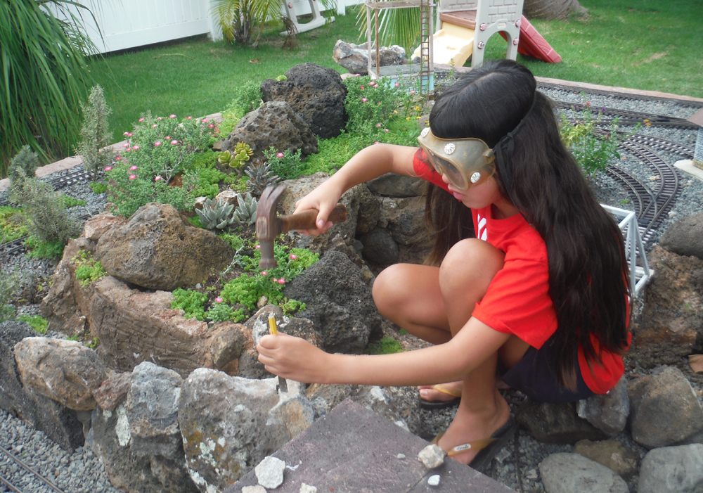 girl works in garden railway with stones