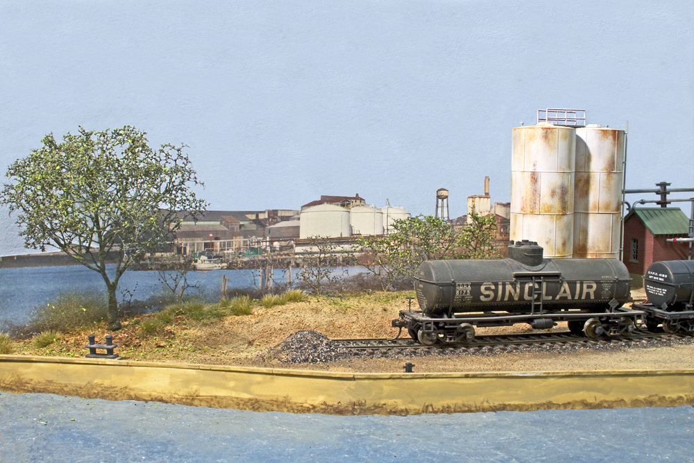 A black tanker car along the waterfront, in front of two white slios and a blue sky background