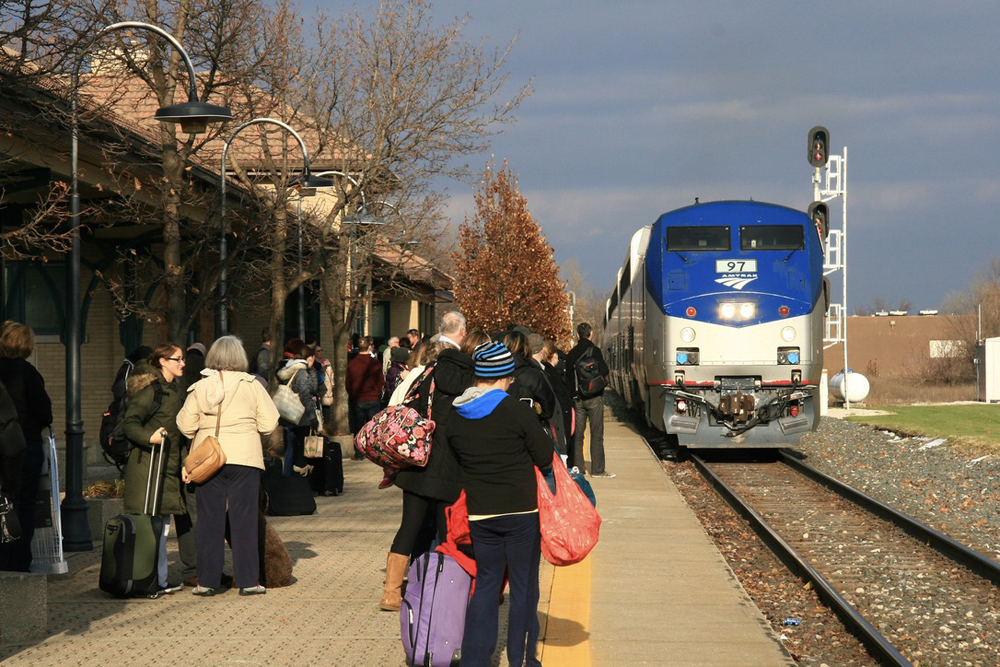 Train approaches full station platform in afternoon sunlight