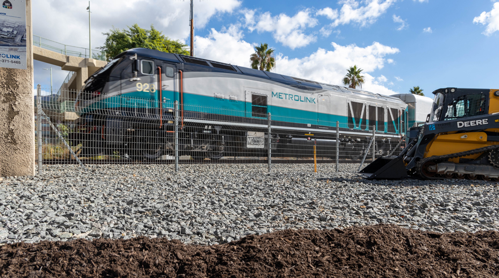 Teal, silver, and black locomotive passes bulldozer