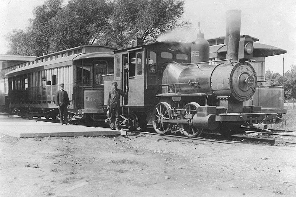 Men stand in front of steam locomotive and passenger car