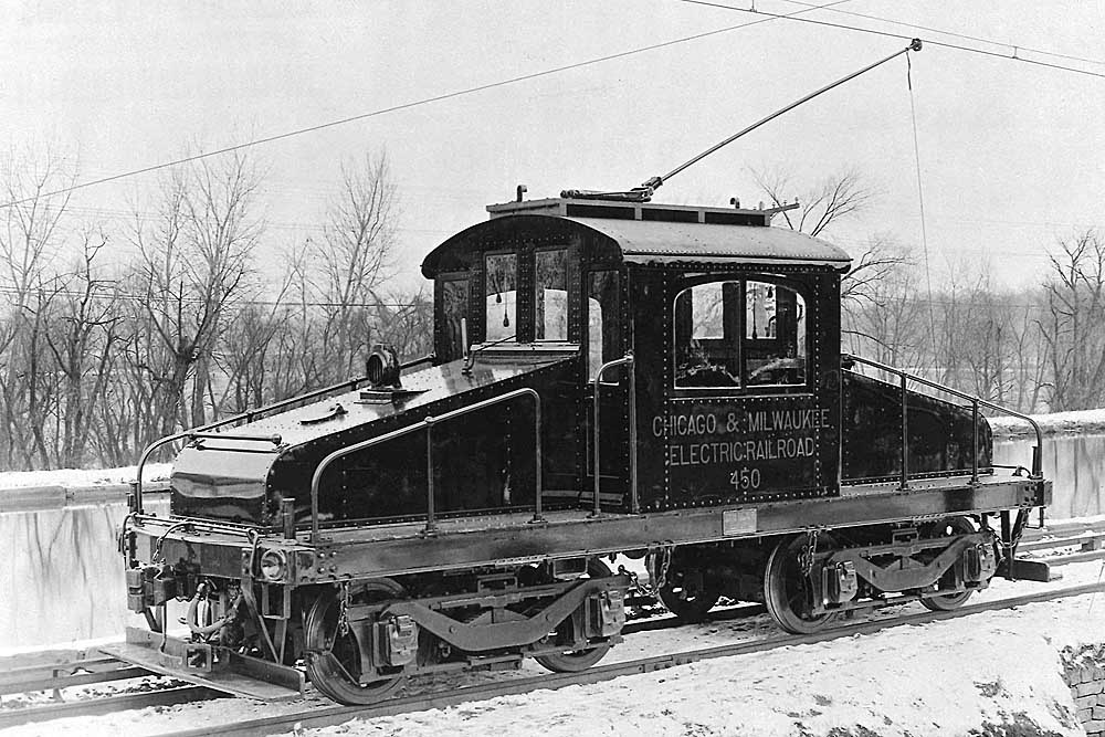 Black centercab electric locomotive with trolley pole raised