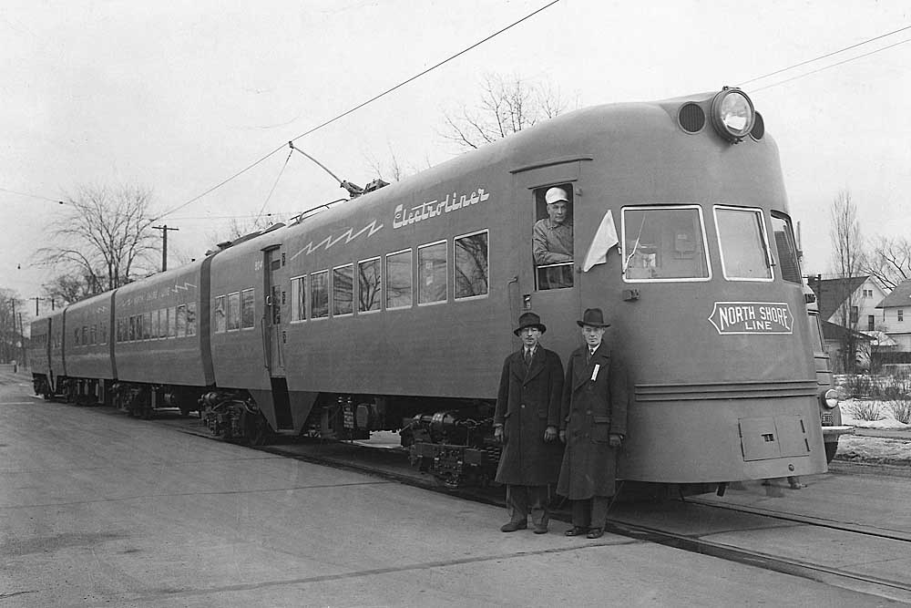 Two men stand in front of electric Chicago North Shore & Milwaukee equipment in street