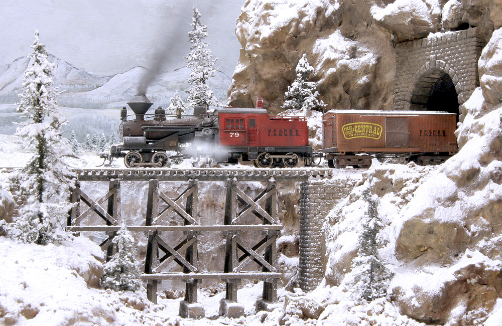A Heisler pulling a boxcar emerges from a tunnel onto a wood trestle above a snowy gorge
