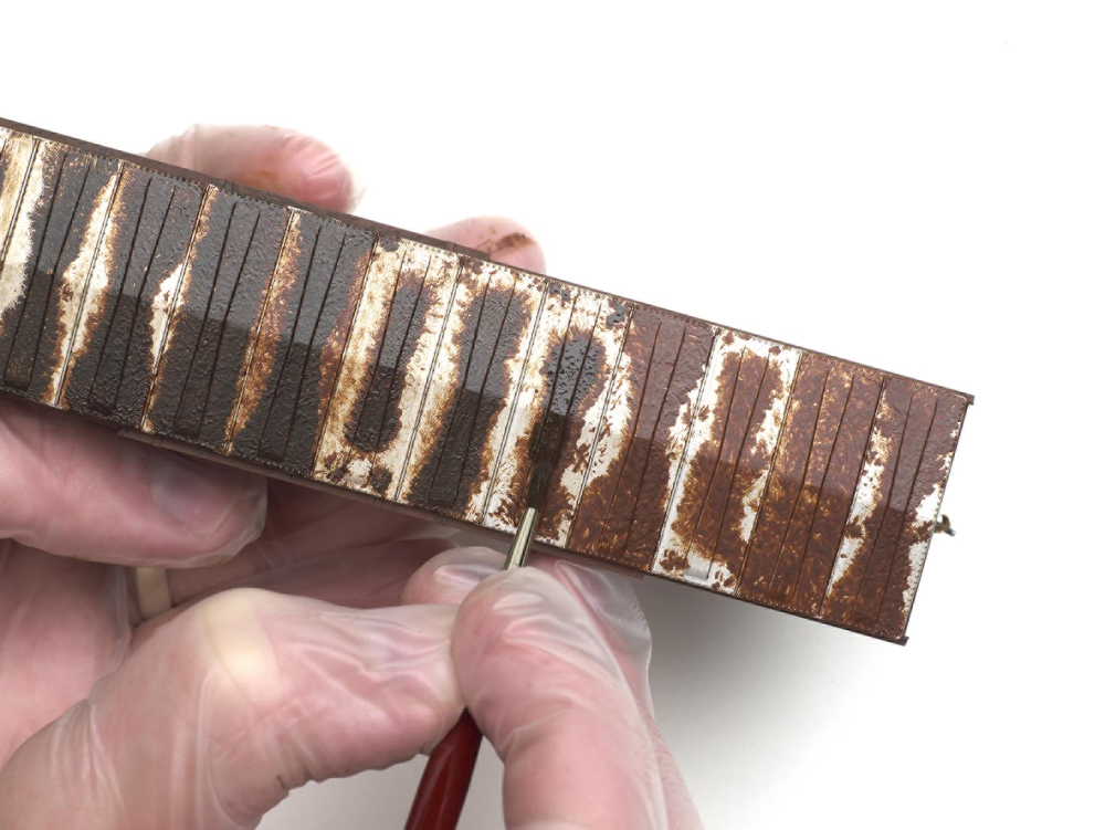 Weathering with artist's oils: A brush is used on the roof of a brown model boxcar to weather.