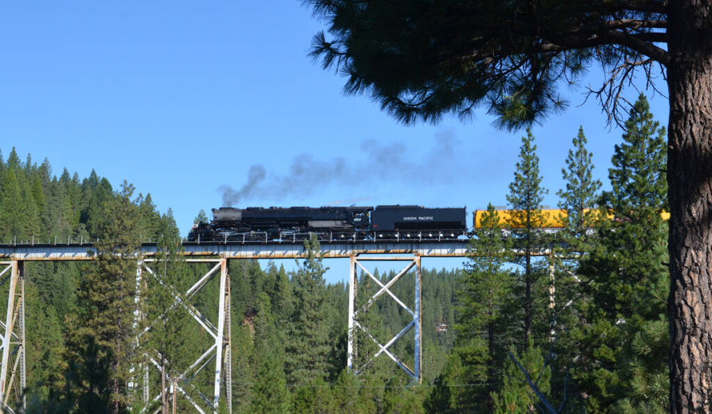 A steam locomotive leads a train over an elevated trestle bridge