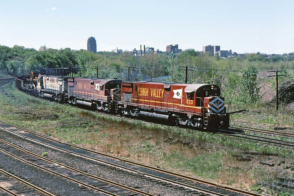 Red-and-yellow and white-and-black on freight train in curve with city skyline