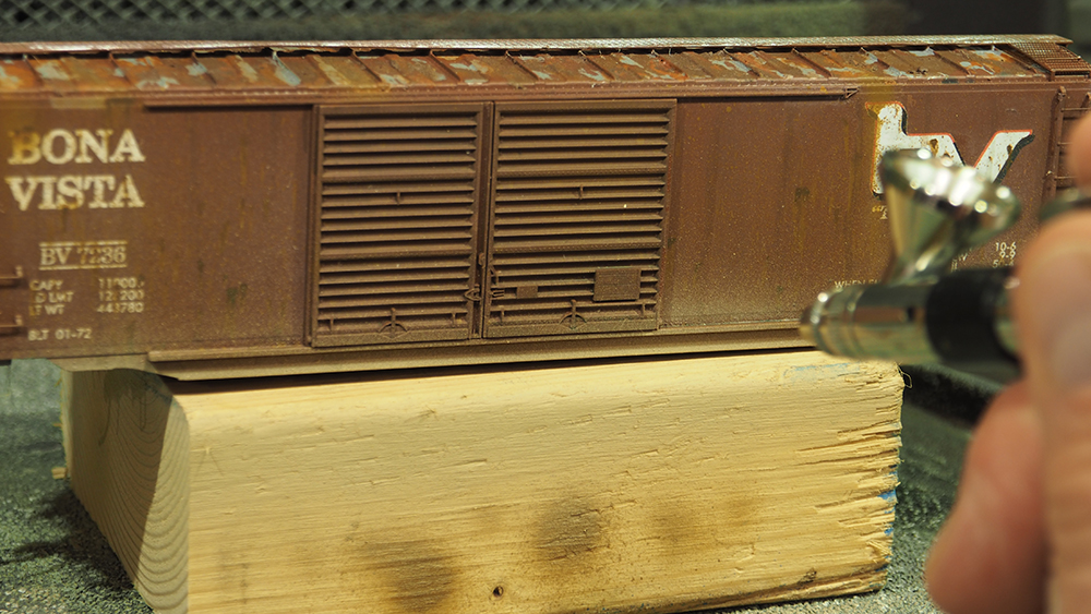 Car Swap Project part 7: Gerry’s creative touch: Silver airbrush applying tan paint to brown model boxcar.